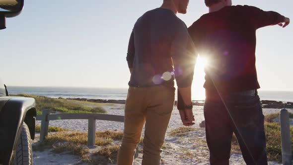 Rear view of caucasian gay male couple holding hands and talking on sunny day at the beach