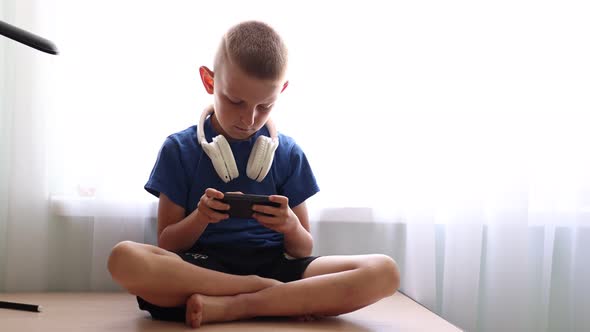 Child's dependence on a mobile device theme. Child with headphones on neck is sitting on table 
