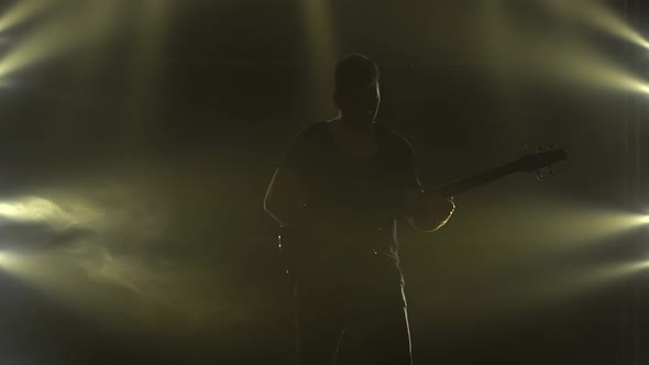 Silhouette of a Young Guy Playing on the Electric Guitar on Stage in a Dark Studio with Smoke and