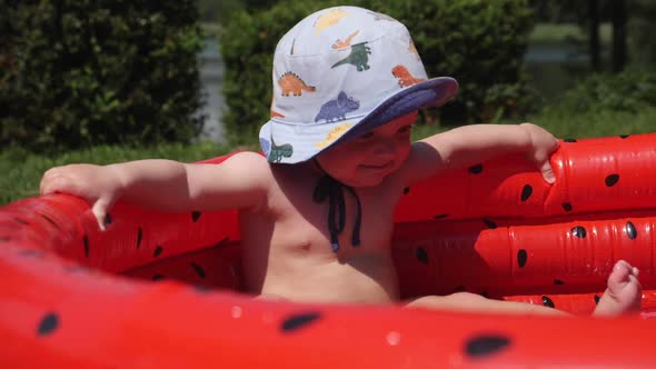 Cute Baby in Bucket Hat Relaxing in Inflatable Watermelon-style Swimming Pool. High Quality FullHD
