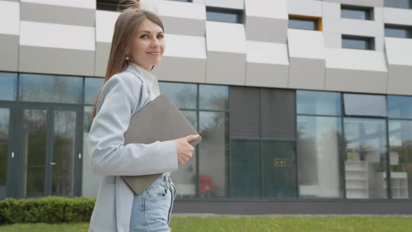 A Girl in a Business Suit with a Laptop in Her Hands Walks Down the Street