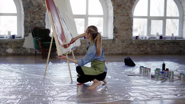 Artist Working with Large Paintbrush and Wide Canvas in Workshop Standing on Knees