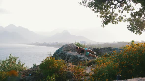 Young Woman Doing Fitness Exercises on Open Air  Leaning on the Rocks and Does Push Ups