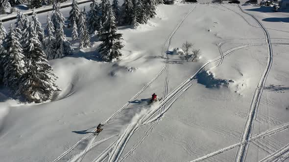 Aerial of snowmobile towing skier who jumps over small hill in snowy landscape. Winter fun activity,