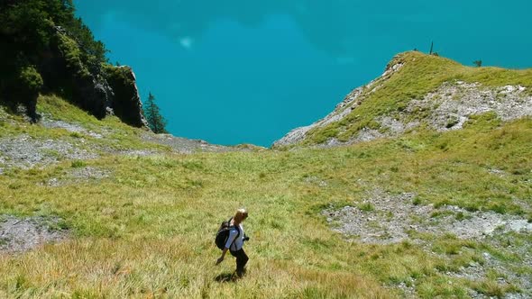 A blonde girl hikes down a Mountain at lake oeschinen in the swiss apls with the blue mountain lake