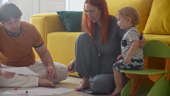 Family with Little Baby Drawing on the Paper Sitting on the Floor