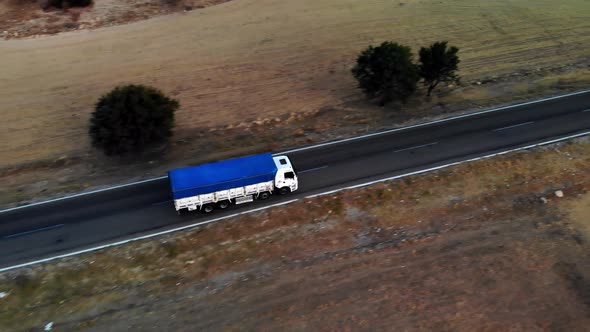 Aerial View of White Truck with Blue Body Driving on Public Roads Between Sand and Dirt Fields