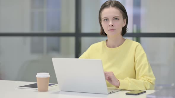 Young Woman Looking at Camera While Using Laptop in Office