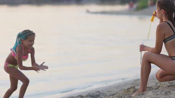 Funny Girl Catches Bubbles on the Shore of the Lake Which Her Older Sister Lets Go