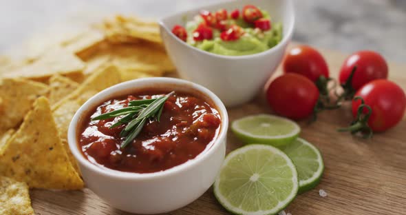 Close up of nachos and sauces on wooden tray on black surface