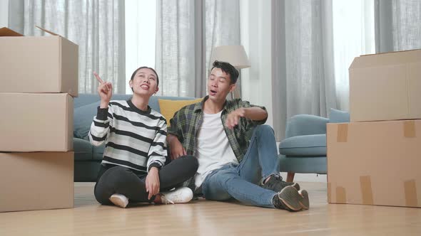 Young Asian Couple With Cardboard Boxes Sit On The Floor And Discuss About The New House