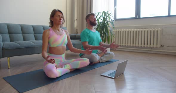 Couple Meditating at Home Inin Front of Laptop with Online Yoga Tutorial