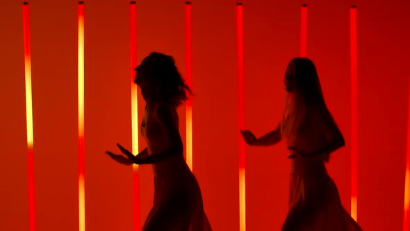 Two Graceful Young Women Practice the Elements of Salsa Dance in a Dark Studio Against a Background