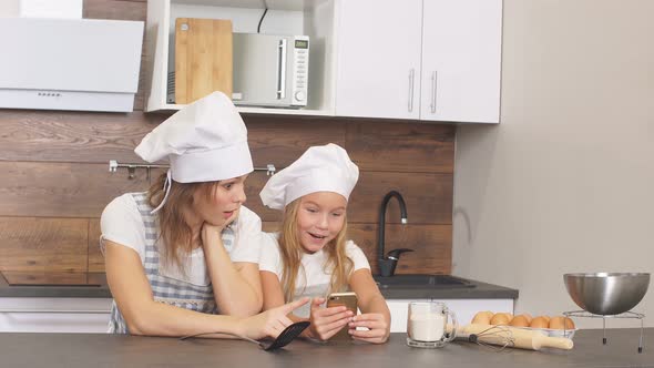 Adorable Happy Sisters Dressed As Chefs Browse Through Various Pie Recipes on Their Smartphone