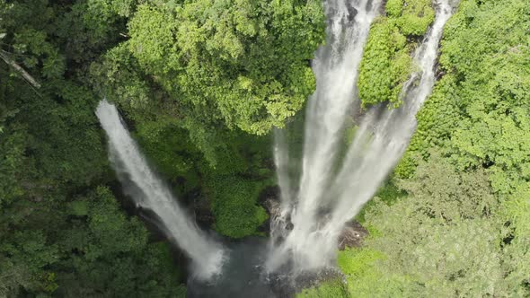 Descending drone of lush jungle waterfall with water mist in sunlight