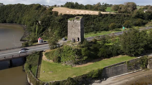 Drone shot of an old castle ruin revealing a busy road and bridge as well as a wide river estuary.