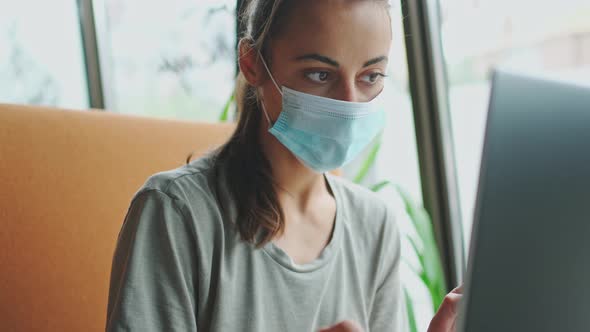 Pensive Woman in Protective Mask Using Laptop