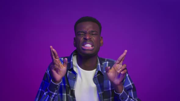 African American Man Crossing Fingers For Luck Over Purple Background