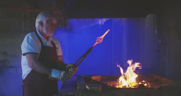 Strong Blacksmith Putting Metalwork in Fire in Furnplace
