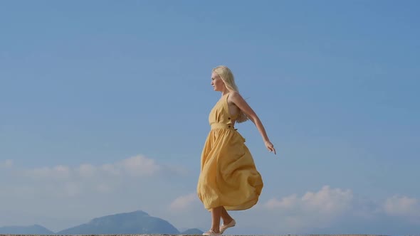 Dancing blonde woman in a yellow dress  against the background of mountains in Montenegro.