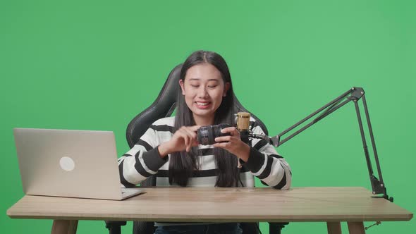 Asian Woman With Computer Reviewing Camera Len While Sitting In Front Of Green Screen
