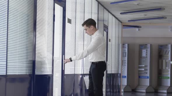 Man Walks Down a White Glass Corridor in an Under Construction Office Building