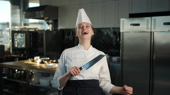 Professional kitchen, portrait: Female Chef holding a knife and laughing ominously