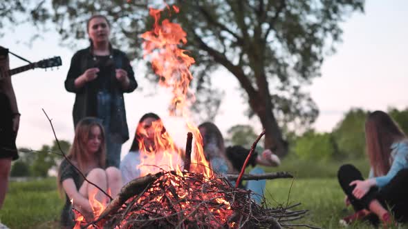 A Group of Friends with a Guitar are Sitting Around the Fire in the Evening