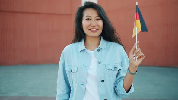 Slow Motion Portrait of Cheerful Asian Woman Holding German Flag Outdoors