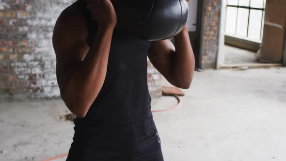 Shirtless african american man exercising with medicine ball in an empty urban building