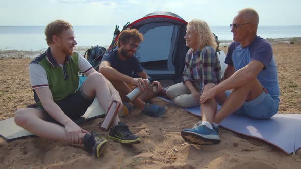 Cheerful Family Camping on Beach Sitting on Sleeping Mats, Talking and Laughing