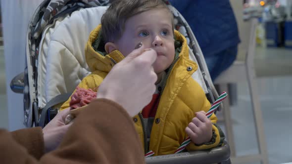 Mom feeds a little boy in a stroller with ice cream in a cafe