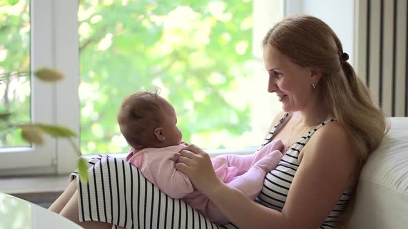 Woman Playing and Kissing Toddler Girl Sitting on Sofa in Home Room Spbd