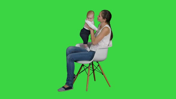 Mother and Cute Baby Sitting on a Chair on a Green Screen, Chroma Key.