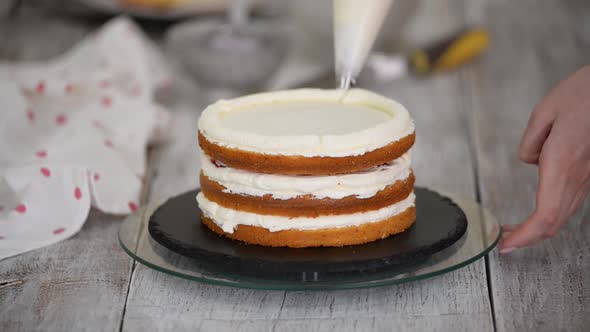 Confectioner with Pastry Bag Squeezing Cream on Cake at Kitchen