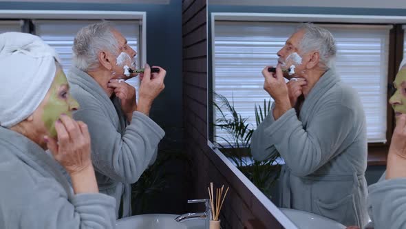 Senior Grandmother Applying Facial Mask and Grandfather Shaving with Manual Razor Blade at Bathroom