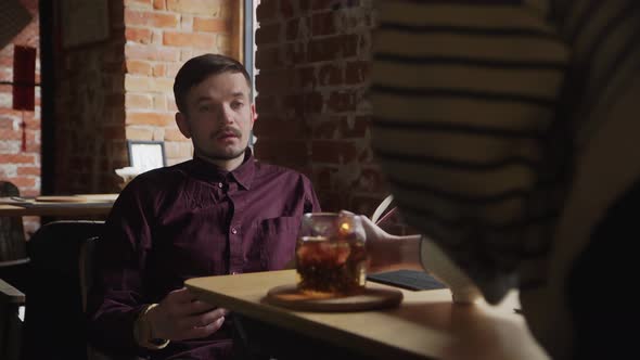 Waiter Brings Tea to Man Which Reading a Book at Cafe