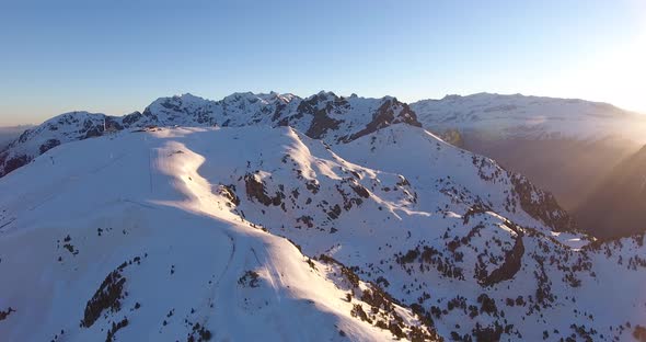 Snowed Alps summit in the Chamrousse peaks in France with sunrise rising, Aerial pan left shot