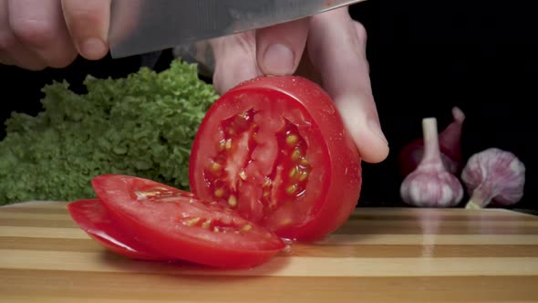 Hands of Man with Knife Slicing Red Tomato Into Rings