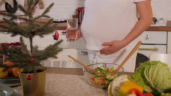 Closeup of a Pregnant Woman Holding a Glass of Water in the Kitchen