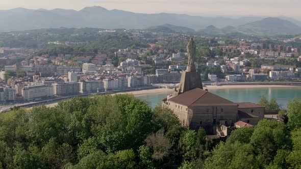 Monument statue with city of San Sebastian in background, cinematic aerial drone view