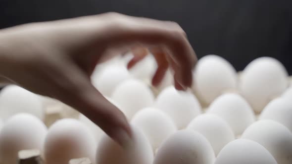Hand puts eggs in a box. Eggs are stacked in a tray.