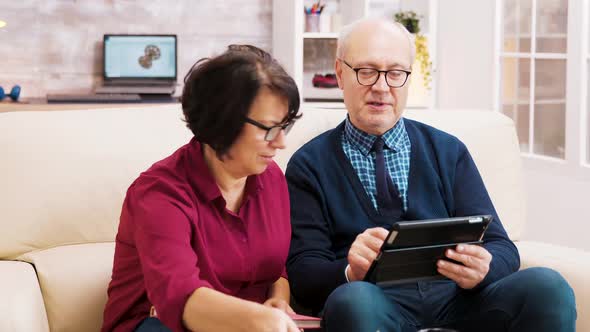 Elderly Age Couple Using Tablet While Sitting on Sofa