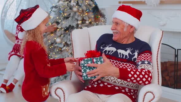 Granddaughter Gifting Christmas Xmas Present Box to Amazed Happy Grandfather at Home Celebrating