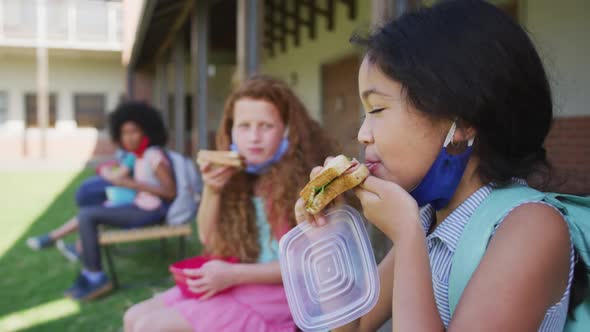 Two girls eating lunch from tiffin box while sitting on bench in the park at school