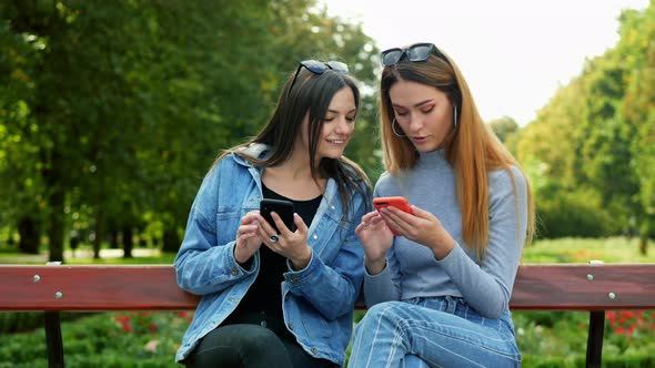 Two Women Friends Sitting on a Bench in Park and Using Mobile Phone, Choosing Pictures