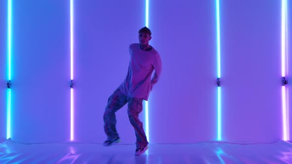 Stylish Young Man with Tattoos Performs Cool Street Dance Against Backdrop of Bright Neon Lights