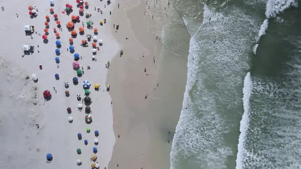 Waves rolling into white sand beach full of tourist in Cabo Frio, Rio de Janeiro, Brazil. Aerial Top