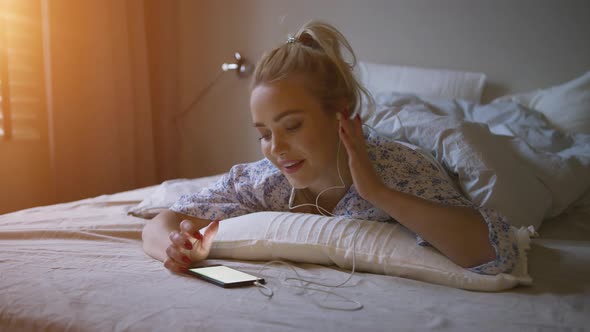 Charming Young Woman with Ponytail Listening To Good Music While Lying on Comfortable Bed