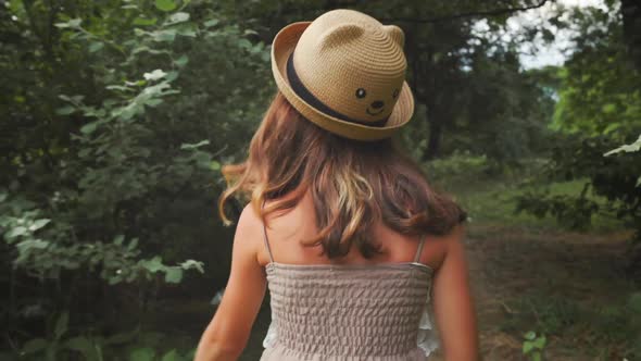 Summer holidays. Back view of little girl in a straw hat and dress running skipping in the park